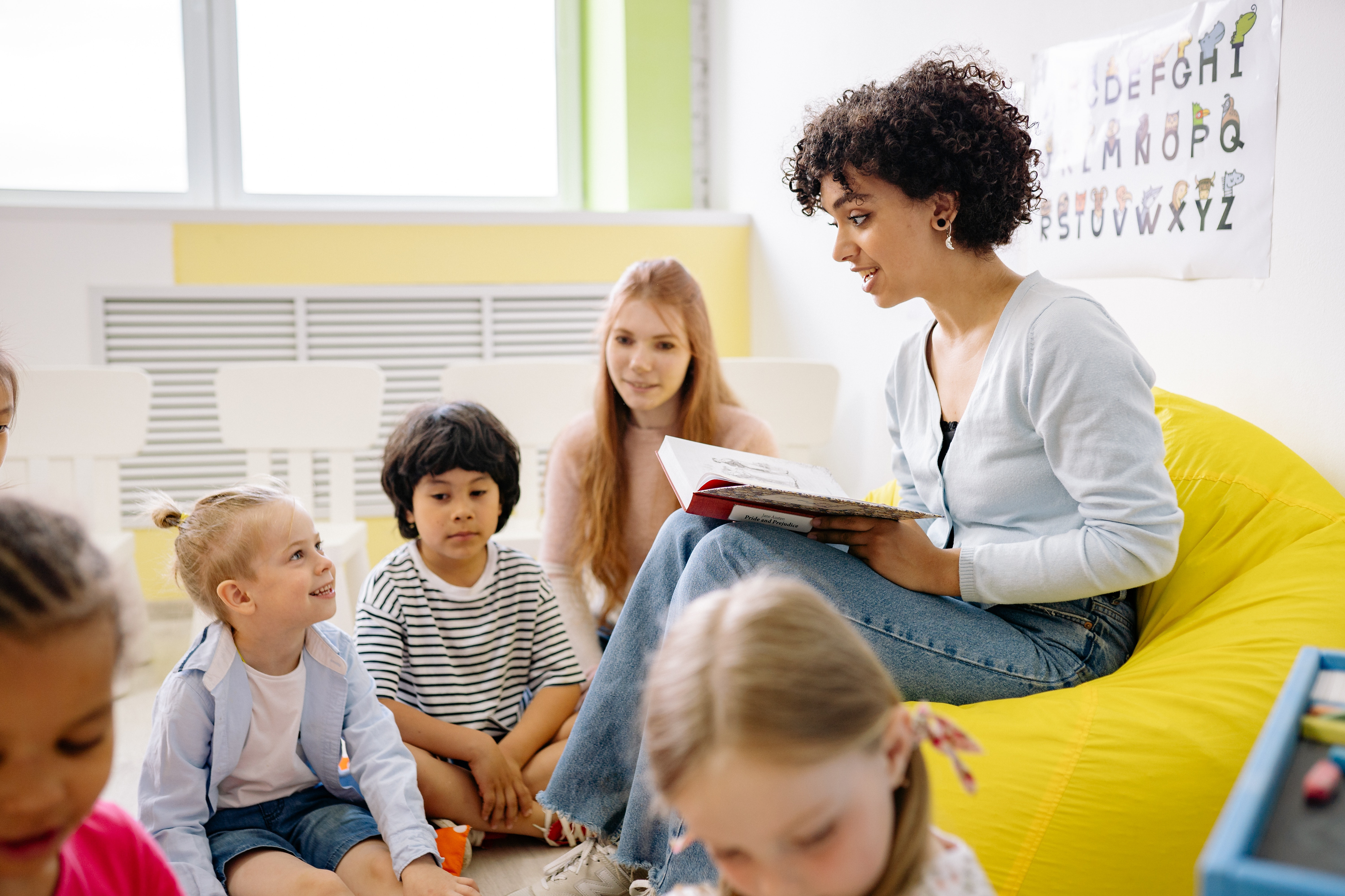 Image of a teacher reading to a group of young students seated on the floor