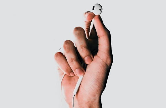 a hand holds up an Apple earbud